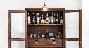 Un meuble bar en bois, doté de plusieurs étagères, d’un porte-verres à vin et d’un petit objet noir placé sur l’étagère inférieure.