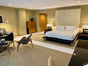 A modern hotel room with a large bed, a sofa, a chair, a desk, and a nightstand with lamps. - Vila Valverde Design and Country Hotel (Lagos)