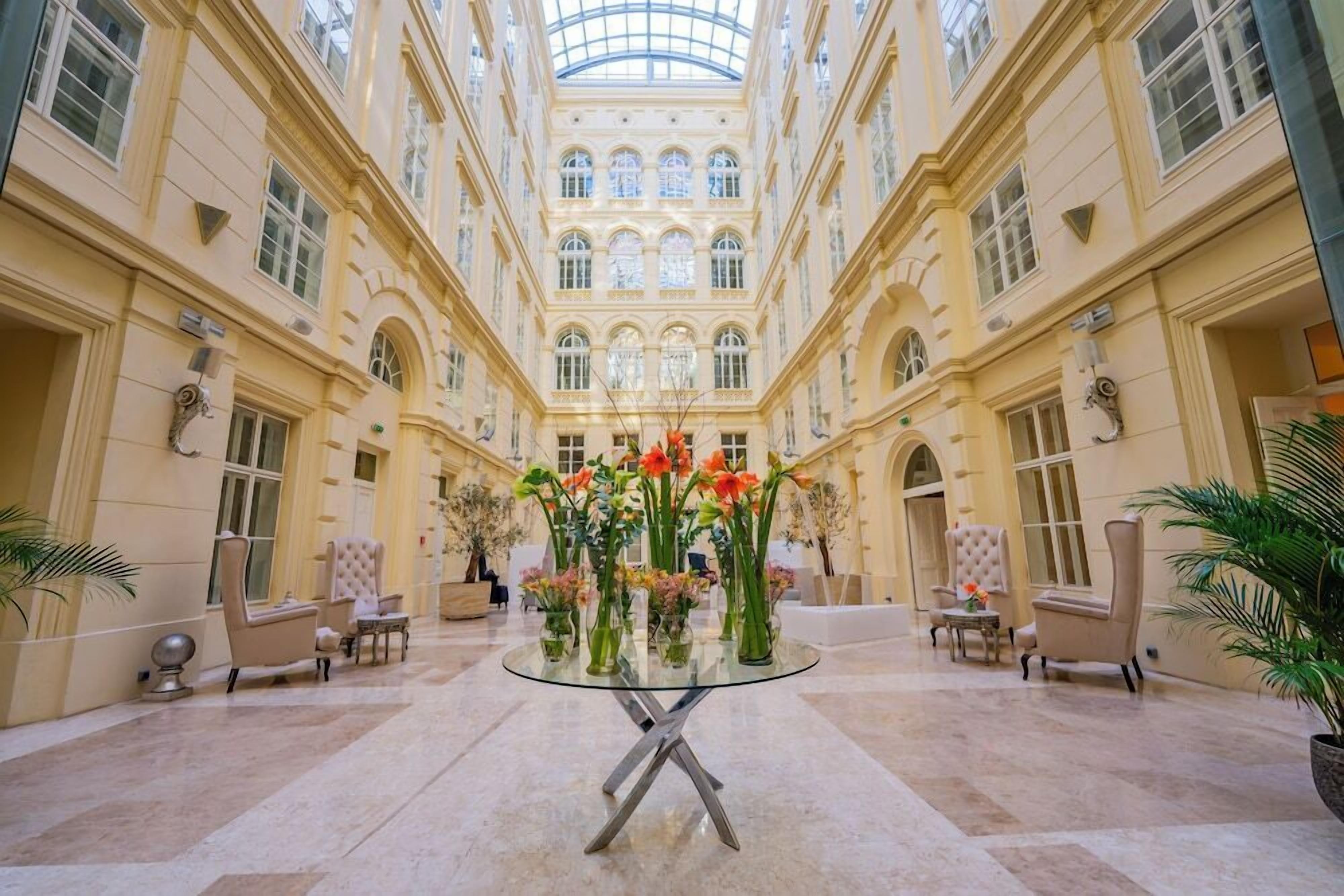 Un vaste atrium doté d’une table à plateau de verre entourée de chaises, d’un arrangement floral central et d’un haut plafond orné de fenêtres en arc de cercle.