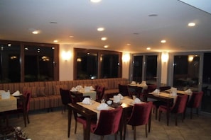Ein Restaurant mit gedeckten Tischen, einer Sofaecke und großen Fenstern.