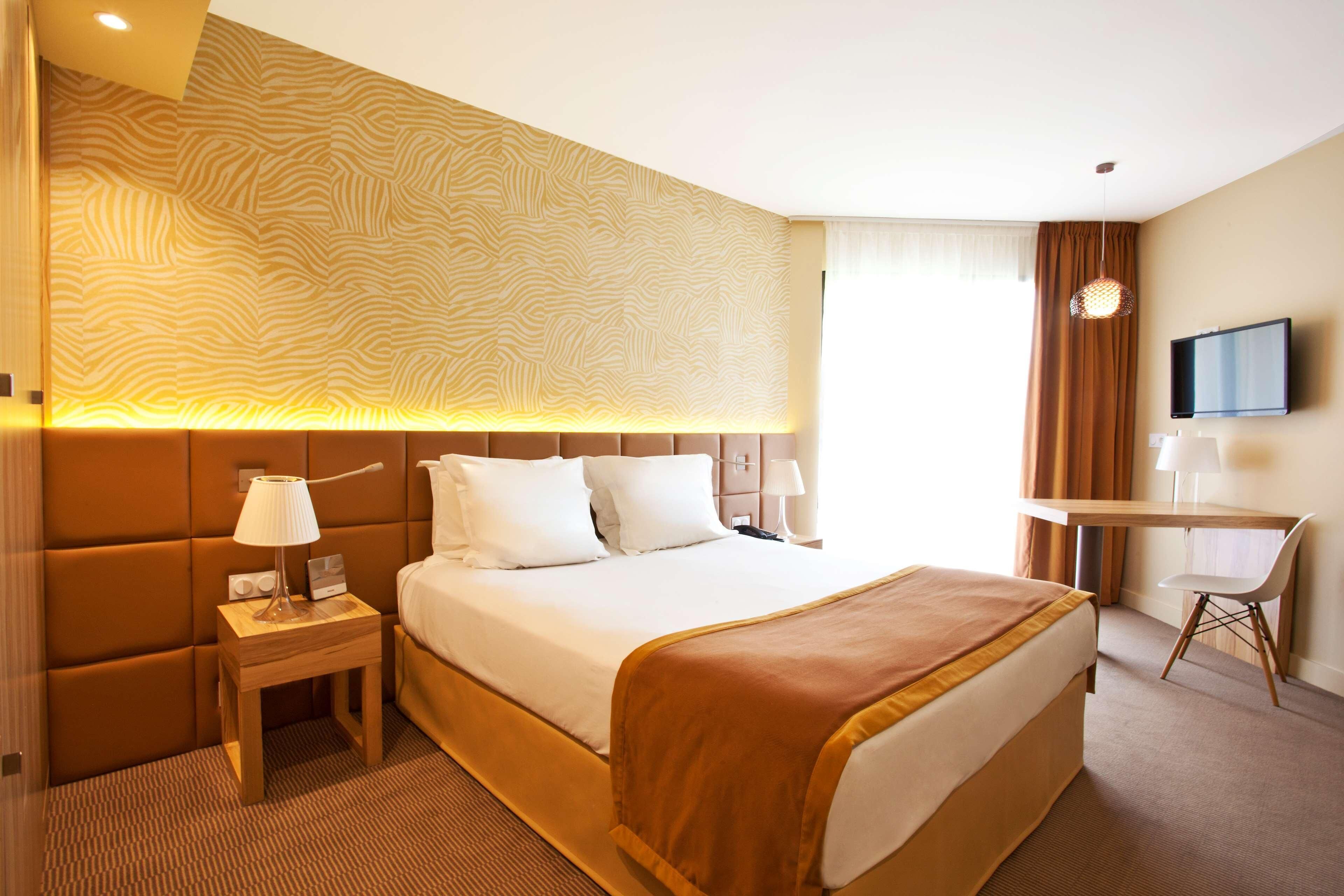 Une chambre d’hôtel comprenant un lit, une table de chevet, une lampe, une télévision et un bureau avec une chaise.