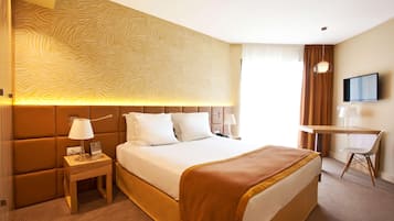Une chambre d’hôtel comprenant un lit, une table de chevet, une lampe, une télévision et un bureau avec une chaise.
