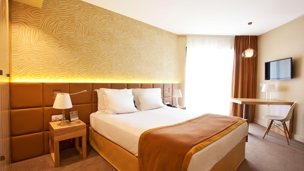 A hotel room with a bed, bedside table, lamp, TV, and a desk with a chair. - Hotel Paradou (Avignon)