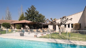A swimming pool with a covered patio area, a fenced yard, and a building with a sloped roof. - Hotel Paradou (Avignon)