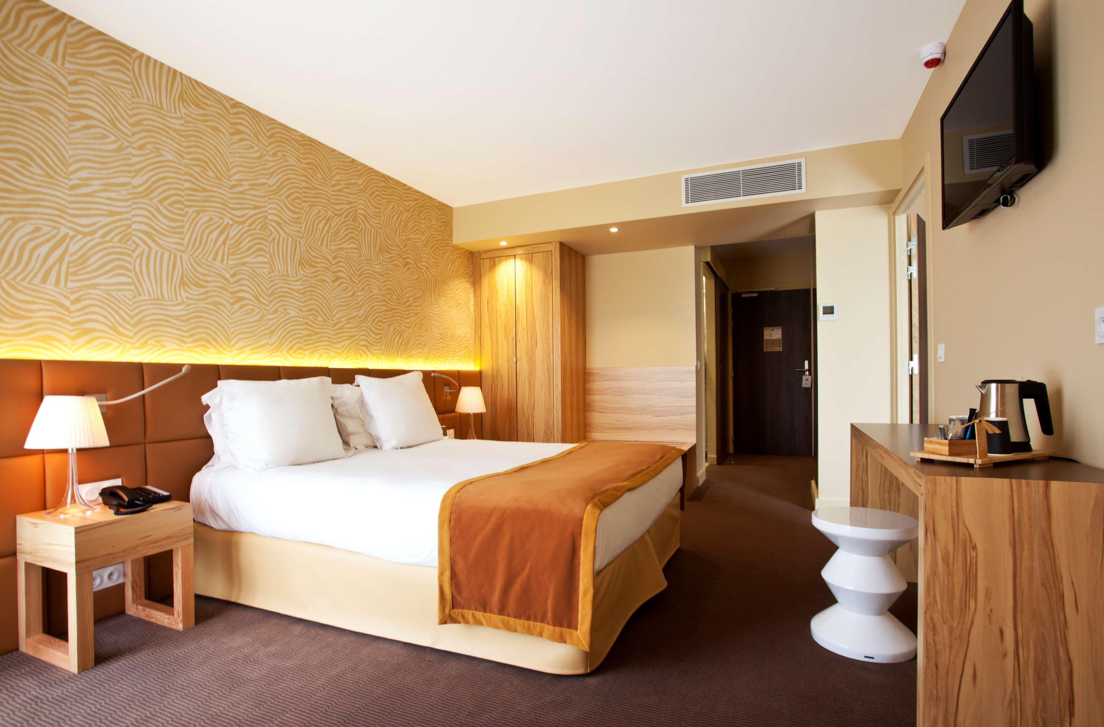 Une chambre d’hôtel avec un lit, une table de chevet, une lampe et un téléviseur posé sur un meuble.