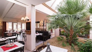 Un restaurant doté d’une salle à manger intérieure, d’une plante centrale et d’un plafond haut.