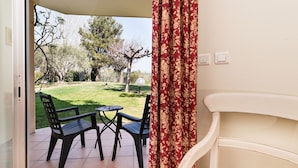 An open patio with a table and chairs, a view of a garden with trees and a lawn, and a white wall with a curtain. - Hotel Paradou (Avignon)