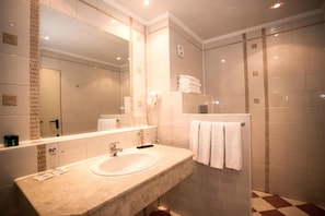 A bathroom with a sink, mirror, towel rack, and tiled walls. - Hotel Royal Bay (Nessebar)