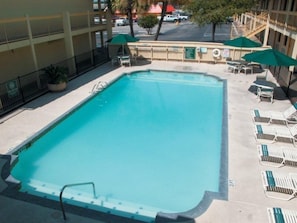 A rectangular pool with a diving board, surrounded by lounge chairs and umbrellas, with a building in the background. - LA Quinta INN SAN Antonio I 35 N AT Rittiman Road (San Antonio)