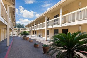 A multi-story hotel with balconies, a courtyard with potted plants, and a clear sky. - LA Quinta INN SAN Antonio I 35 N AT Rittiman Road (San Antonio)