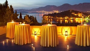 A terrace with round tables, candles, and a view of a lake and mountains at dusk. - Croatia Hotel (Konavle)