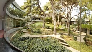 A modern building with a curved glass facade, a landscaped garden with trees and a pathway, and a reflective floor. - Croatia Hotel (Konavle)