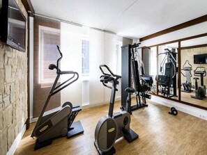A home gym with exercise equipment, a large mirror, and a stone wall. - Suite Novotel Hamburg City (Hamburg)