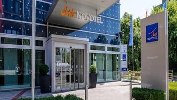 Una entrada de hotel moderna con puertas de vidrio, un letrero que dice 'Suite Novotel Hamburgo' y un letrero de estacionamiento.