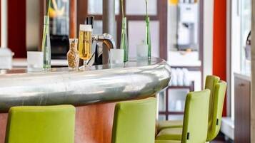 Una zona de bar con una barra curva, sillas verdes y diversos utensilios.
