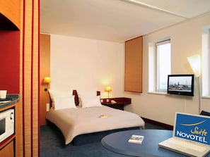 A hotel room with a bed, bedside lamps, a TV, a laptop, and a minibar. - Suite Novotel Hamburg City (Hamburg)