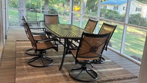 Een overdekt terras met een tafel, stoelen, grote ramen en een plafondventilator.