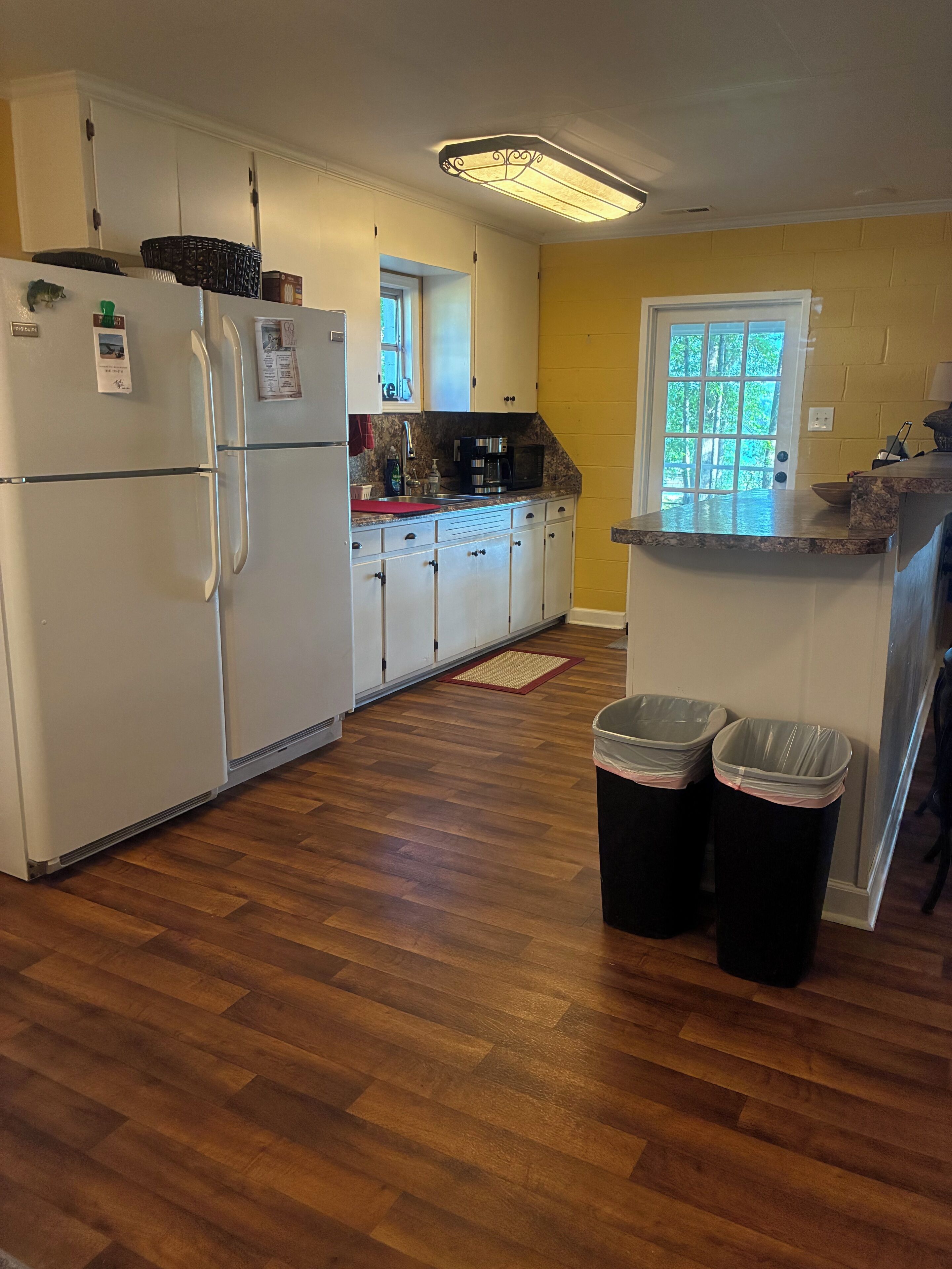 A kitchen with white cabinets, a microwave, a refrigerator, and two trash bins.