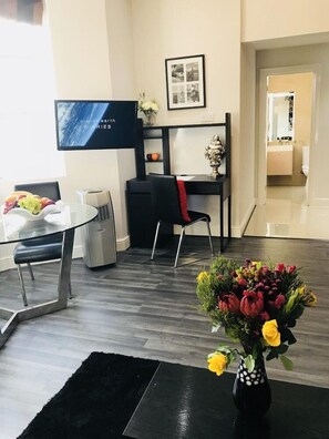 Una sala de estar moderna con una televisión de pantalla plana, una mesa de comedor con sillas, un sofá negro y un jarrón de flores.
