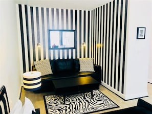 Una sala de estar moderna con un sofá negro, paneles en la pared a rayas, un alfombra con estampado de cebra y una pequeña mesa redonda.