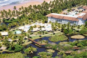 An aerial view of a resort with a large building, multiple swimming pools, and a dense palm tree area. - Sauipe Pousadas (Mata de São João)