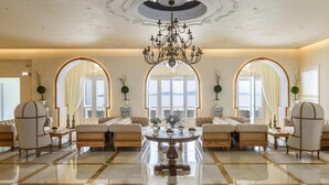 A spacious lobby with a chandelier, sofas, a round table, and large arched windows. - Saint John Hotel Villas and Spa (Mykonos)
