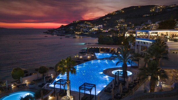 A resort with a large infinity pool, lounge chairs, and a view of the sea at sunset. - Saint John Hotel Villas and Spa (Mykonos)