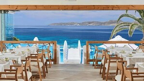 A restaurant with tables and chairs facing a scenic ocean view. - Saint John Hotel Villas and Spa (Mykonos)