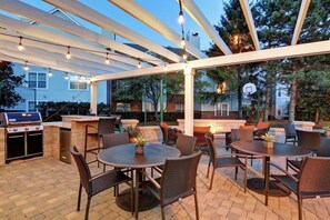 Eine Terrasse im Freien mit Grill, runden Tischen und Korbstühlen.