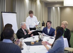 Ein Konferenzraum mit rundem Tisch, Stühlen, einer Whiteboard-Tafel und einer Projektionsleinwand.