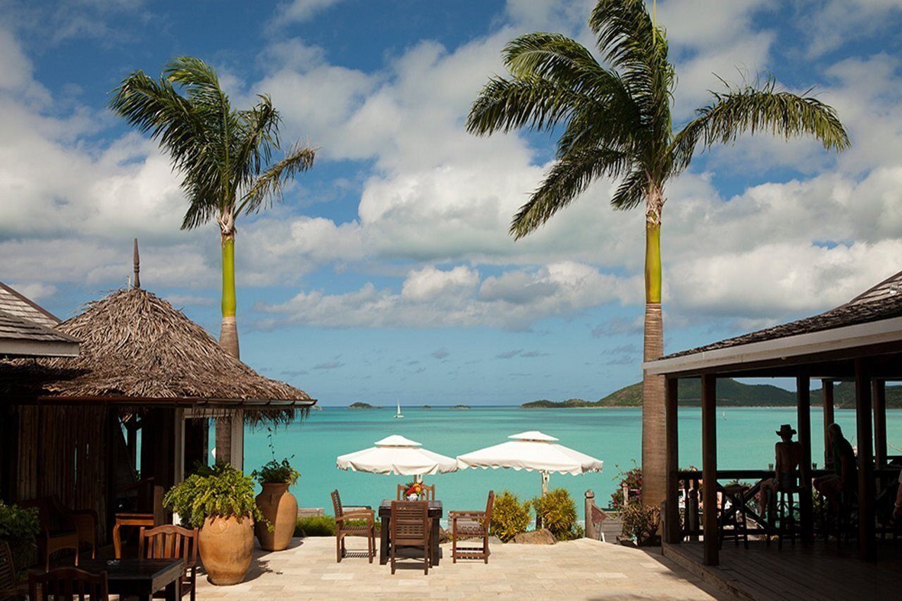 A tropical resort with a thatched-roof structure, outdoor seating with umbrellas, and a view of turquoise waters.