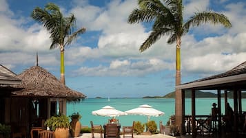 A tropical resort with a thatched-roof structure, outdoor seating with umbrellas, and a view of turquoise waters.