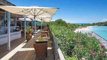 A wooden deck with outdoor seating, umbrellas, and a view of a beach and ocean.