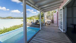 Una terraza de madera con piscina, cerca blanca y vista al mar.