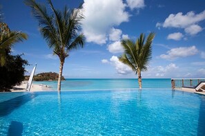 Piscina azul translúcida com palmeiras, uma praia e um céu claro.