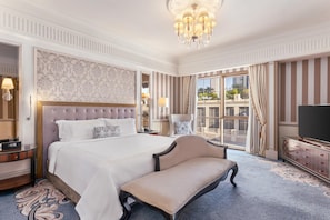 A hotel room with a large bed, a bench, a TV, and a view of the city. - Al Habtoor Palace (Dubai)