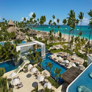 Un resort con piscina, tumbonas, palmeras y vistas al océano.