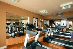Un gimnasio con varias cintas de correr, bicicletas estáticas y elípticas.