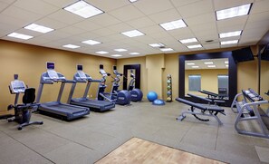 Une salle de sport équipée de tapis de course, de vélos elliptiques, d’un banc de développé couché et de ballons d’exercice.