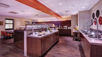 A buffet setup with various food items, a seating area with chairs, and a wooden floor.