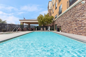 Una piscina con lettini, un muro in pietra e un edificio con una bandiera.