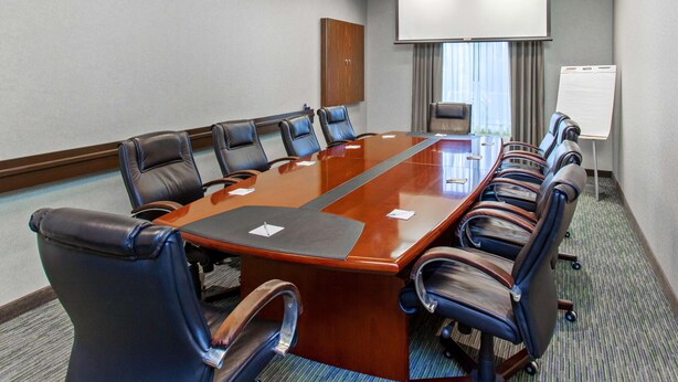 Une salle de conférence équipée d’une longue table, de plusieurs chaises, d’un écran de projection et d’un tableau blanc.