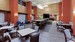 Un hall d’hôtel doté de plusieurs espaces aménagés avec des sièges, notamment des tables et des chaises, et d’un espace central agrémenté d’une cheminée.