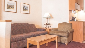 Ein Wohnzimmer mit Sofa, Sessel, Tisch und Lampe. Zwei gerahmte Bilder hängen an der Wand.
