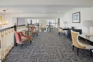 Un amplio hall de hotel con alfombra estampada, zonas de estar, una escalera y un comedor.