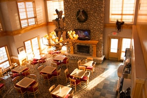 A dining area with tables and chairs, a stone fireplace, and a television screen. - Wingate by Wyndham Elko (Elko)