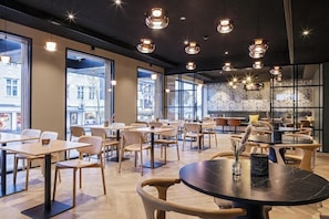 A modern cafe with round tables and chairs, large windows, and pendant lighting.