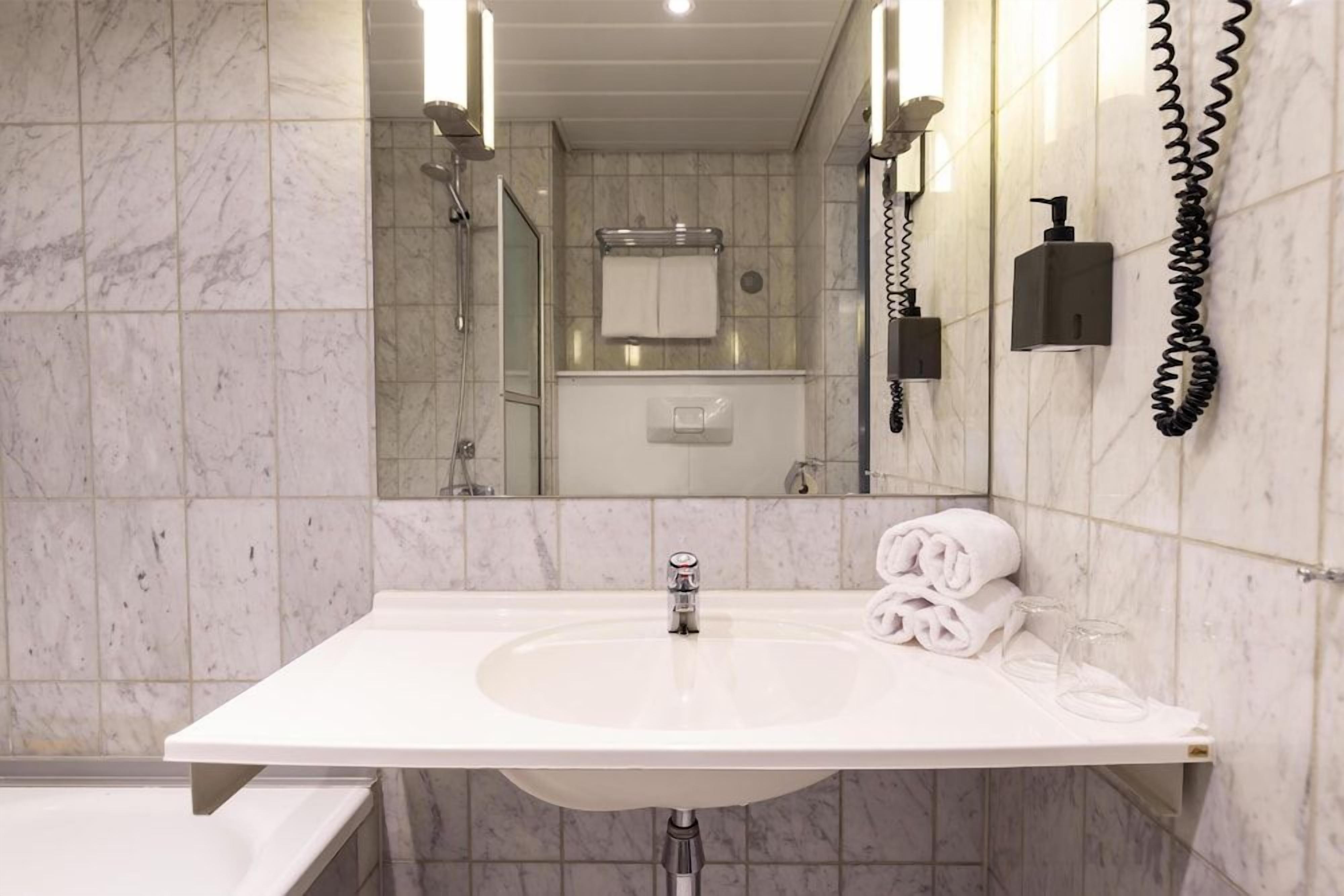 A bathroom with a white sink, a mirror, a towel rack, and a handheld showerhead.