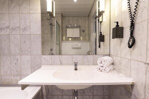 Un baño con un lavabo blanco, un espejo, un perchero para toallas y un cabezal de ducha manual.