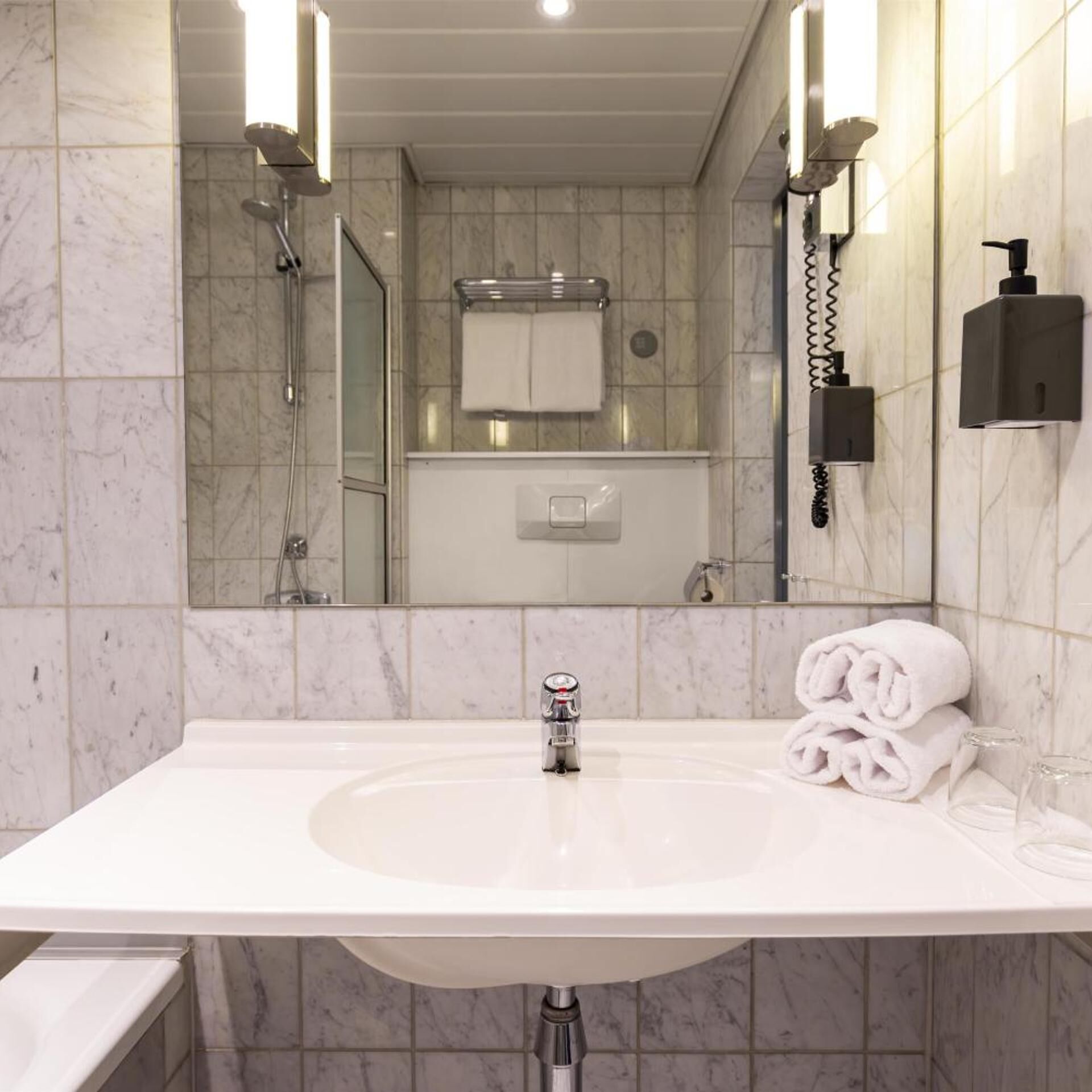 Une salle de bain moderne avec un lavabo blanc, une douche en verre et un porte-serviettes.